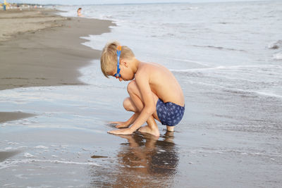 Full length of shirtless boy playing on beach