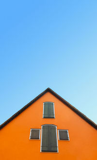 Orange house with pitched roof  on a blue sky. german home with orange walls and timber shutters.