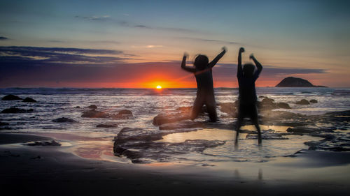 Silhouette people standing on beach against sky during sunset