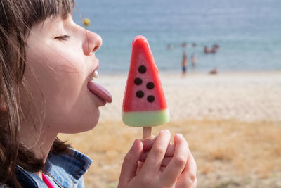 Little girl eating a watermelon ice cream with beach background