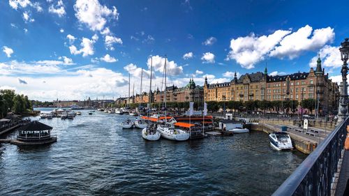 Sailboats moored on river by buildings in city against sky