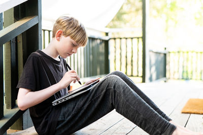 Young person sitting on porch outside using tablet and stylus