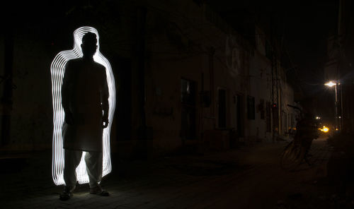 Silhouette man standing against illuminated light in city at night