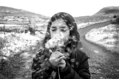 Cute girl with eyes closed blowing dandelions on field