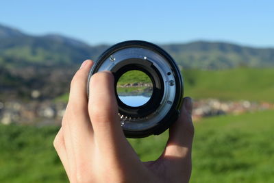 Close-up of hand holding telephoto lens against landscape