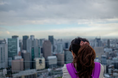 Rear view of woman standing in front of cityscape against sky