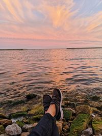 Low section of person on rock by sea against sky