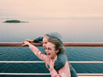 Siblings standing by railing against sea