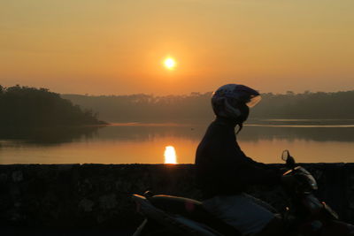 Silhouette man looking at lake against sky during sunset