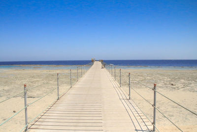 Pier on beach against clear blue sky