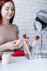 Young beautiful woman holding make-up brushes and making up with cosmetics set at home