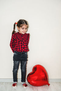 Full length of cute girl with heart shape balloon standing on floor against wall at home