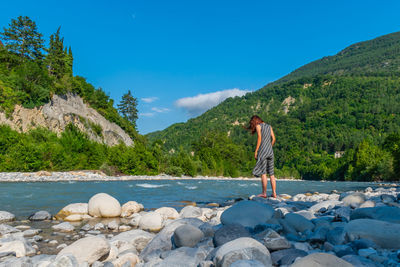 Rear view of man standing on rock against blue sky