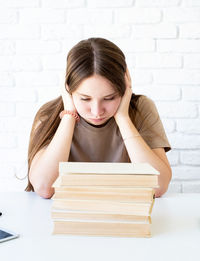 Portrait of a young woman sitting on table against wall