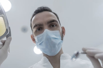 Close-up of doctor wearing surgical mask against white background