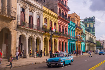 Vehicles on road by buildings in city against sky