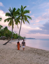 Rear view of woman standing at beach against sky