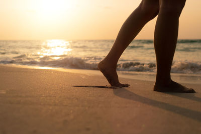 Low section of person on beach against sky during sunset