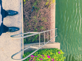 Low section of man standing by ladder leading towards lake