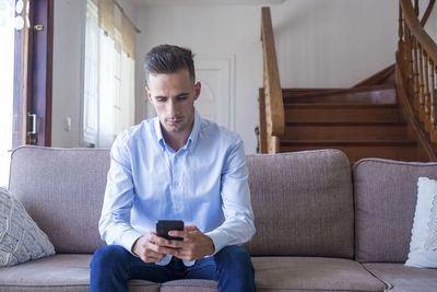 Young man using mobile phone while sitting on sofa at home