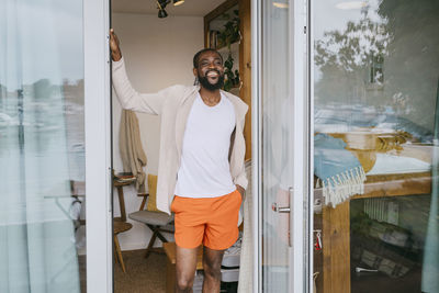 Smiling mature man with hand in pocket standing at doorway