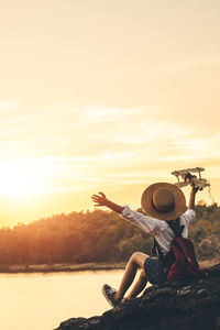 Midsection of woman sitting on land against sky during sunset