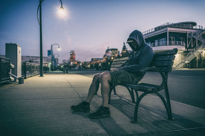 Side view of man sitting in city against sky