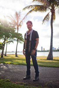 Full length portrait of young man standing on palm tree