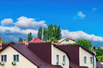 An apartment building with a brown roof against a blue sky with clouds.