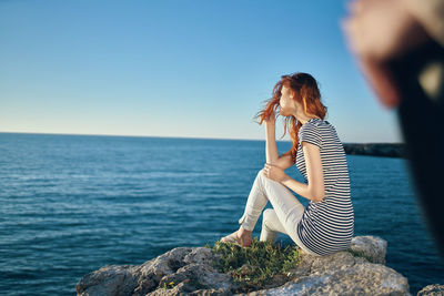 Woman sitting on rock by sea against sky