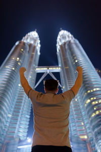 Rear view of man standing against modern buildings at night
