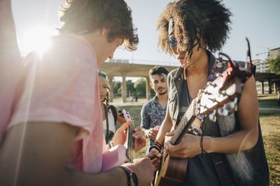 Friends looking at men playing ukulele in concert on sunny day