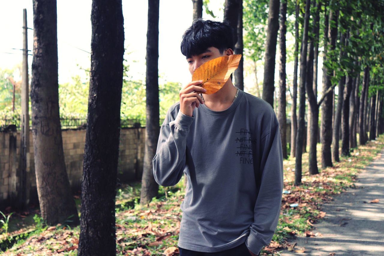 tree, forest, one person, land, standing, trunk, tree trunk, casual clothing, plant, waist up, real people, leisure activity, day, young men, lifestyles, young adult, nature, woodland, front view, outdoors, obscured face