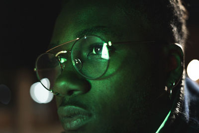 Close-up of man wearing eyeglasses in illuminated city at night
