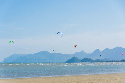 Parachutes flying over sea by mountains against sky