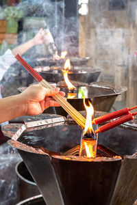 Cropped woman holding burning incense stick in temple
