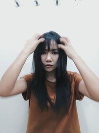 Portrait of woman scratching head while standing against white wall