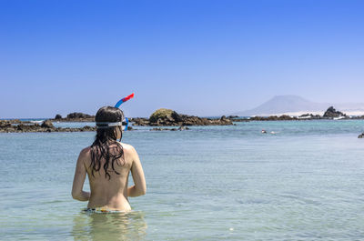 Rear view of shirtless man in sea against clear sky