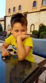 Portrait of boy holding umbrella against building