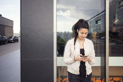 Young woman using smart phone against window