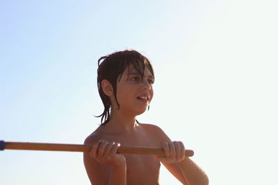 Close-up of wet shirtless boy holding stick against clear sky