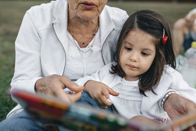 Grandmother showing picture book to granddaughter on meadow