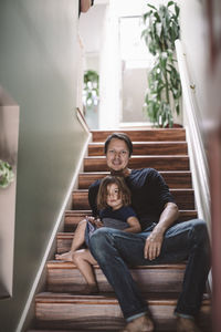 Portrait of smiling father with daughter sitting on steps at home