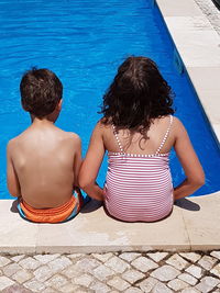 Rear view of siblings sitting in swimming pool