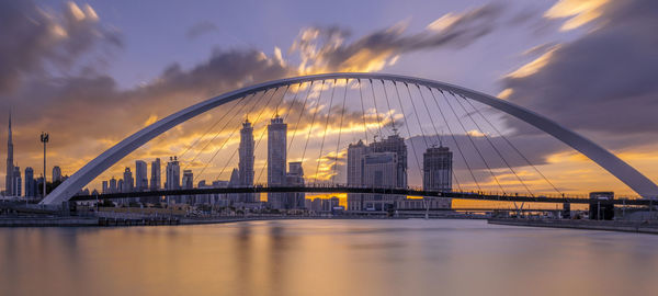 Bridge over river against cloudy sky during sunset