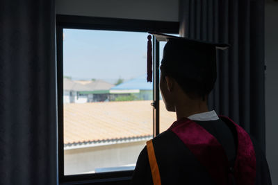 Man in graduation gown looking through window