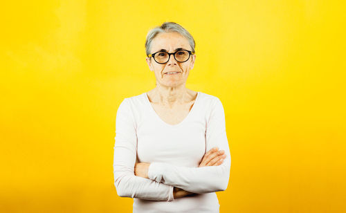 Portrait of young woman standing against yellow background