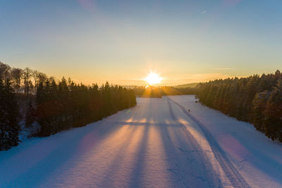 Snow covered landscape against sky during sunset