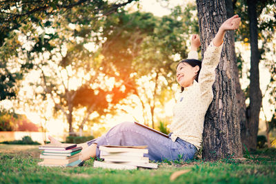 Young woman sitting on book against tree trunk