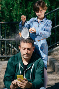 Smiling girl dropping water over fathers head outdoors